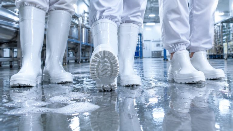 Three workers in tall, mid and short white food safety boots on a wet foamy slaughterhouse floor