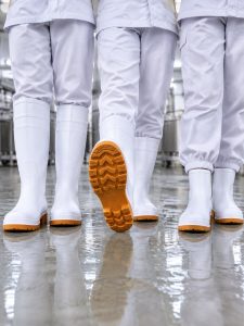 Three food plant workers wearing tall, mid and short white safety boots with anti-slip orange outsoles on a wet floor