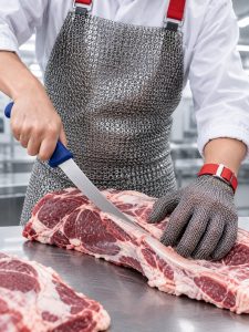 Worker in a chainmail apron and chainmail glove cutting a beef primal with a boning knife